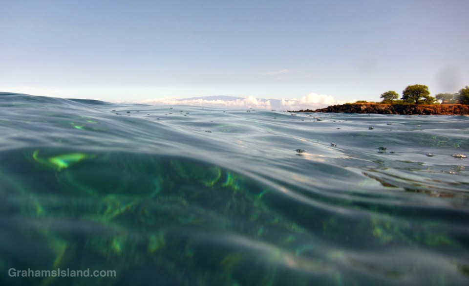 Maui stands out above puffy clouds and long, low swell.