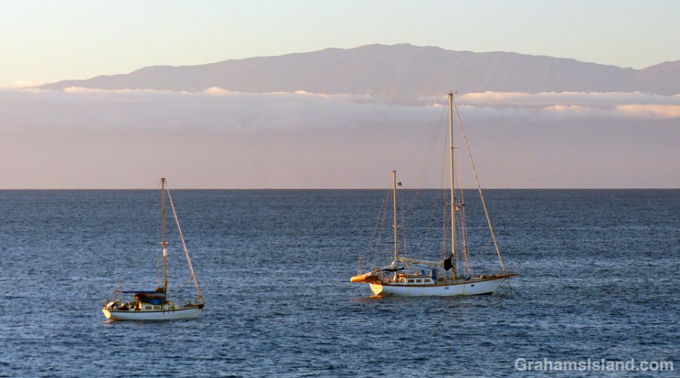 A pair of sailboats at anchor off the Big Island with Maui in the background.