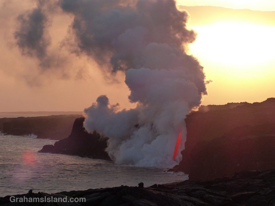 As the sun sinks slowly in the west, a firehose of lava from Kilauea Volcano gushes into the sea.