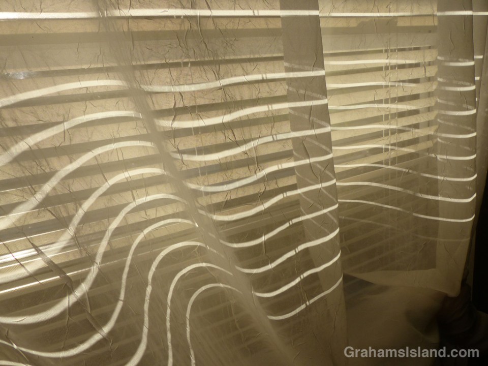 Late afternoon light streams through lowered blinds to create this pattern on the lace curtains inside.