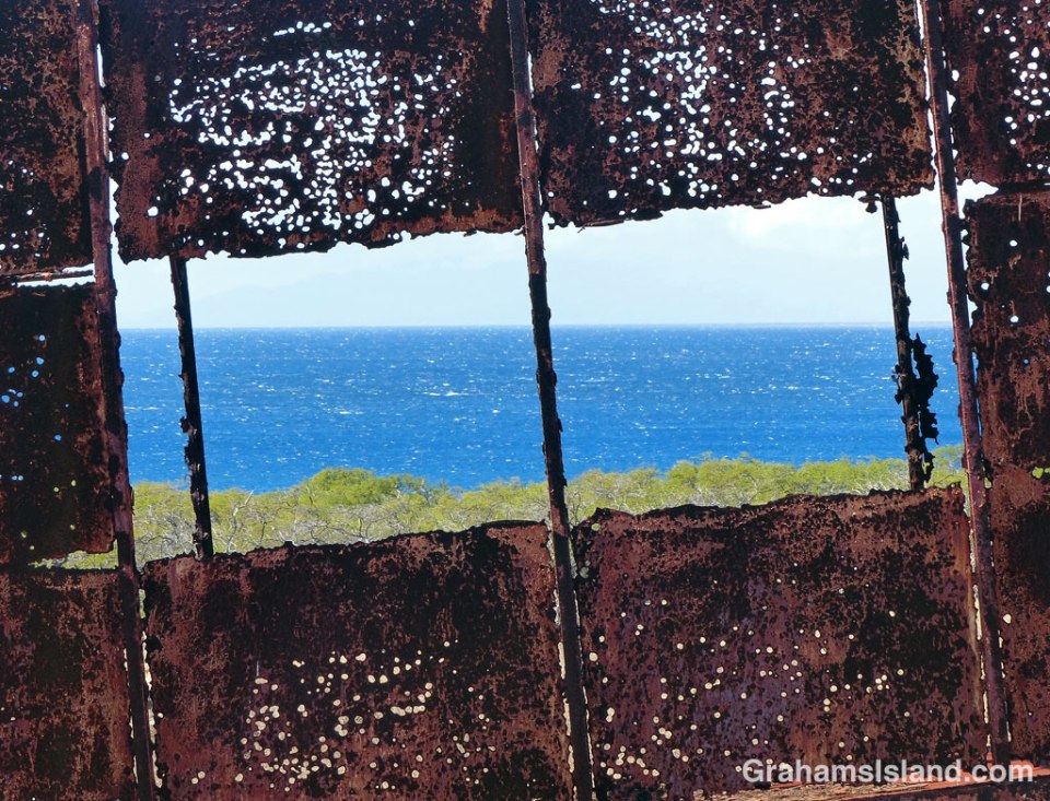 A view of the ocean as seen through a trailer, shot through with rust and perhaps a few bullet holes.