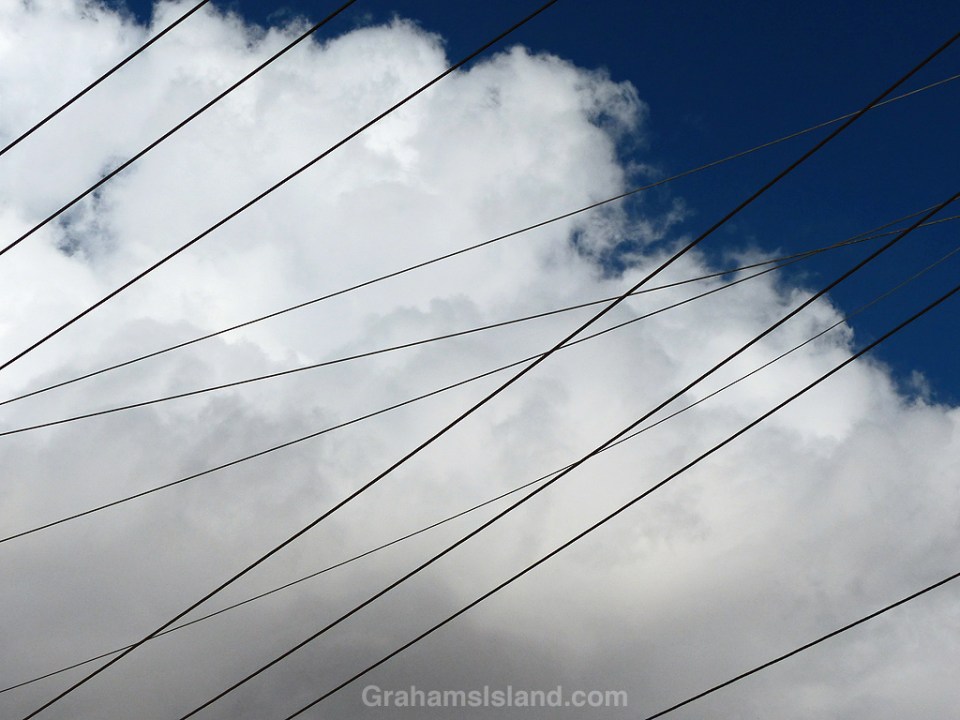 Power lines crisscross beneath fluffy clouds and a deep blue sky.