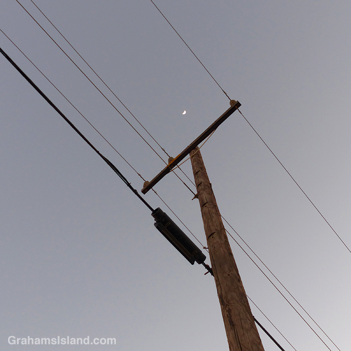 A crescent moon above power lines