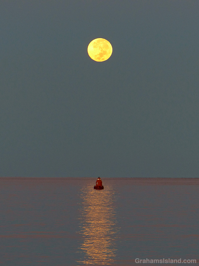 A full moon sets over a red buoy off Kawaihae, Hawaii