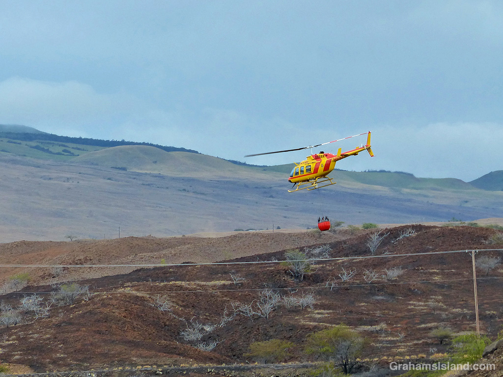 A firefighting helicopter carries water to a brush fire in Hawaii