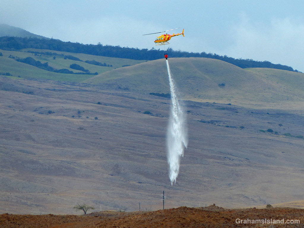 A firefighting helicopter drops water on a brush fire in Hawaii