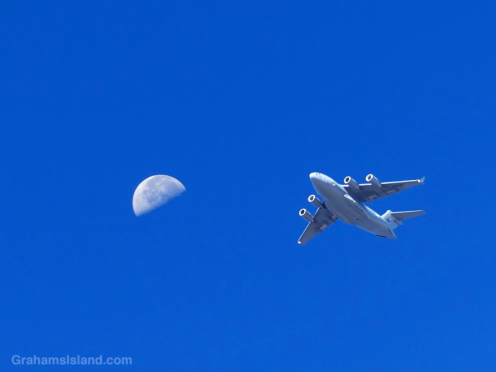 A military plane flying with the moon in the background