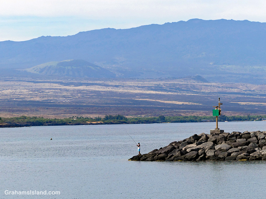 A man fishes from the end of the breakwater at Kawaihae Harbor, Hawaii