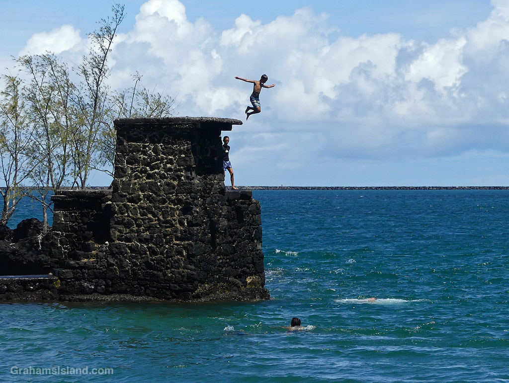 A child jumps into the ocean from a rock tower at Coconut Island, Hilo, Hawaii