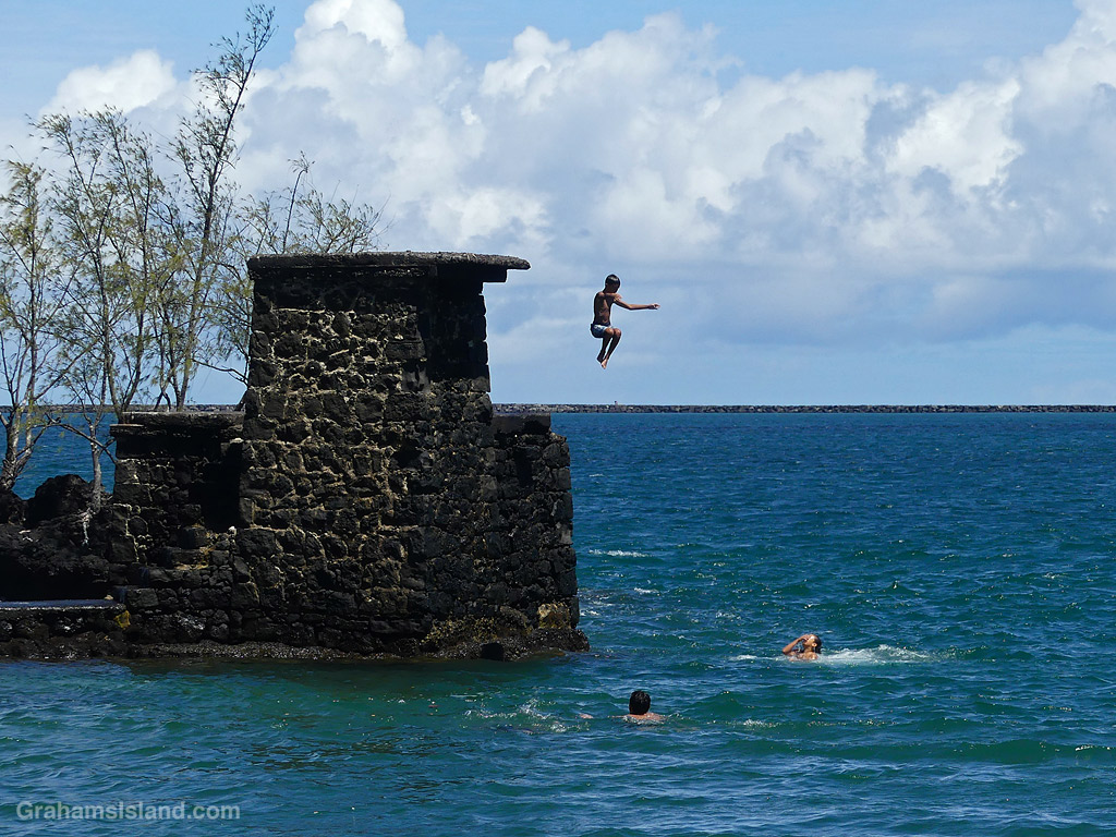 A child jumps into the ocean from a rock tower at Coconut Island, Hilo, Hawaii