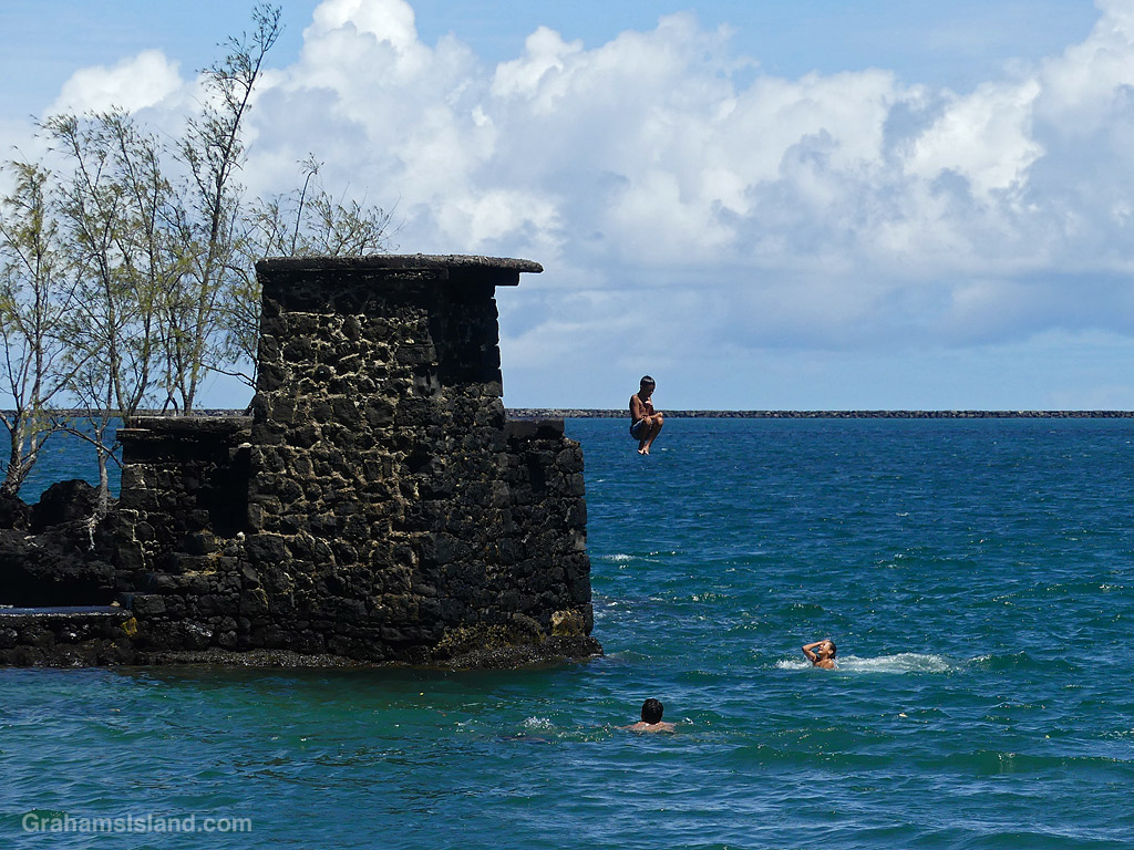 A child jumps into the ocean from a rock tower at Coconut Island, Hilo, Hawaii