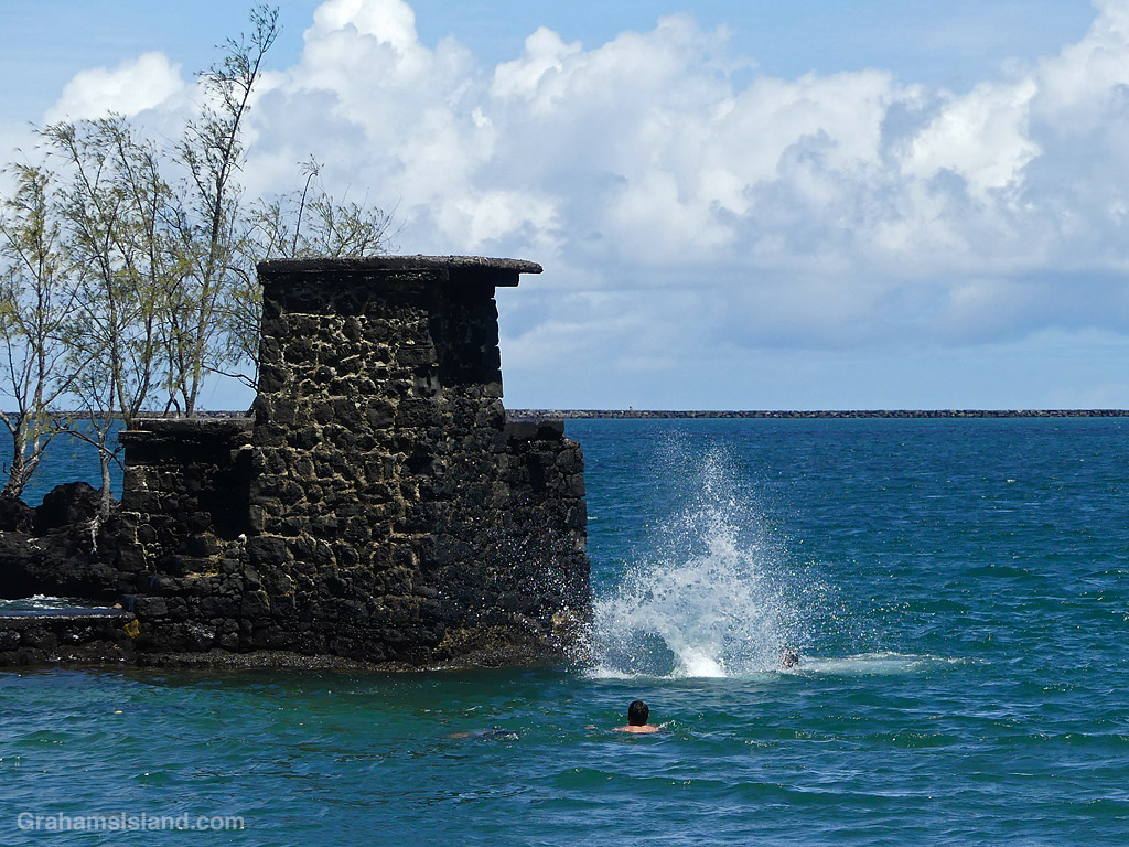 A child jumps into the ocean from a rock tower at Coconut Island, Hilo, Hawaii