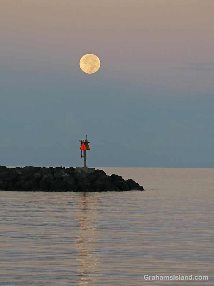 The moon sets over the breakwater at Kawaihae harbor, Hawaii