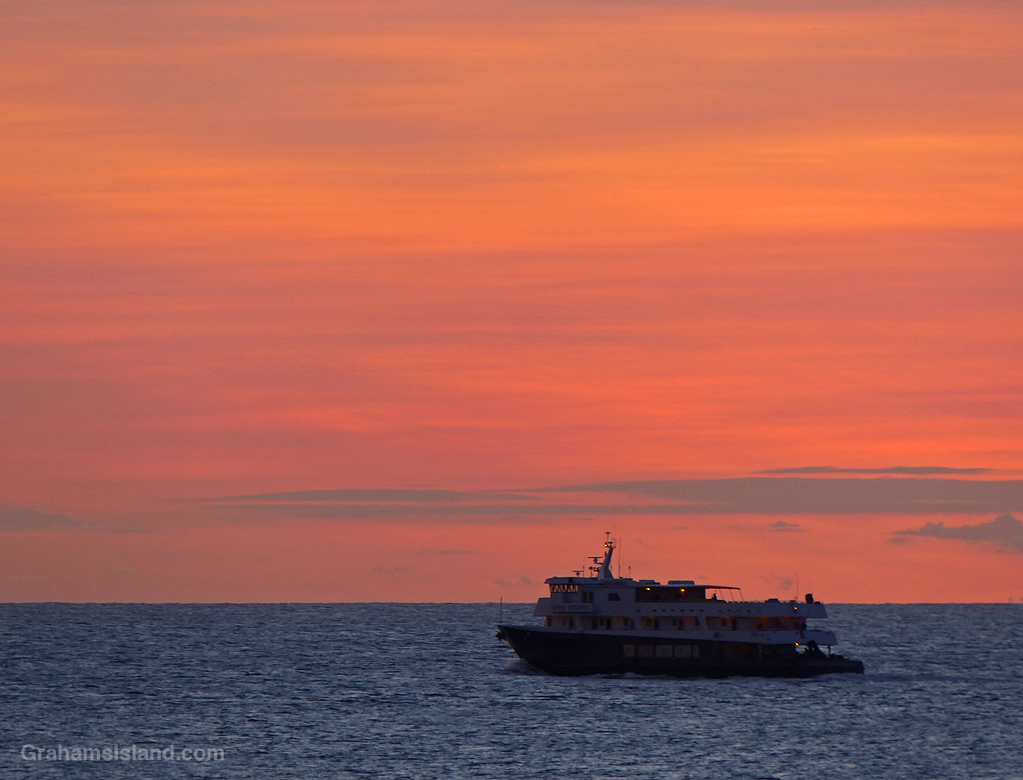 A small cruise ship sails off the coast of the Big Island in Hawaii at sunset